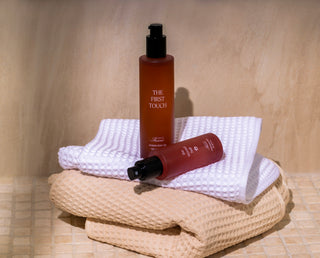 The First Touch body oil and The Second Half pet mist displayed on folded towels as ritual set
