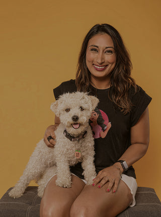 Woman holding small white dog while smiling at camera
