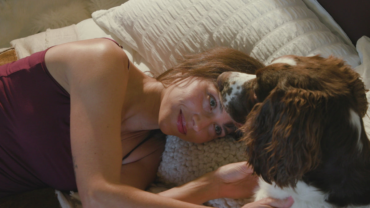 Woman relaxing in bed while dog licks her face in playful moment